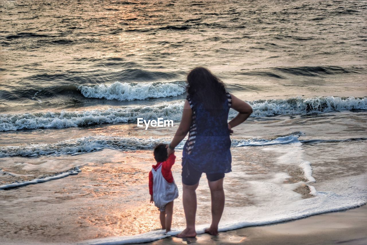 Rear view of mother with daughter standing at beach during sunset