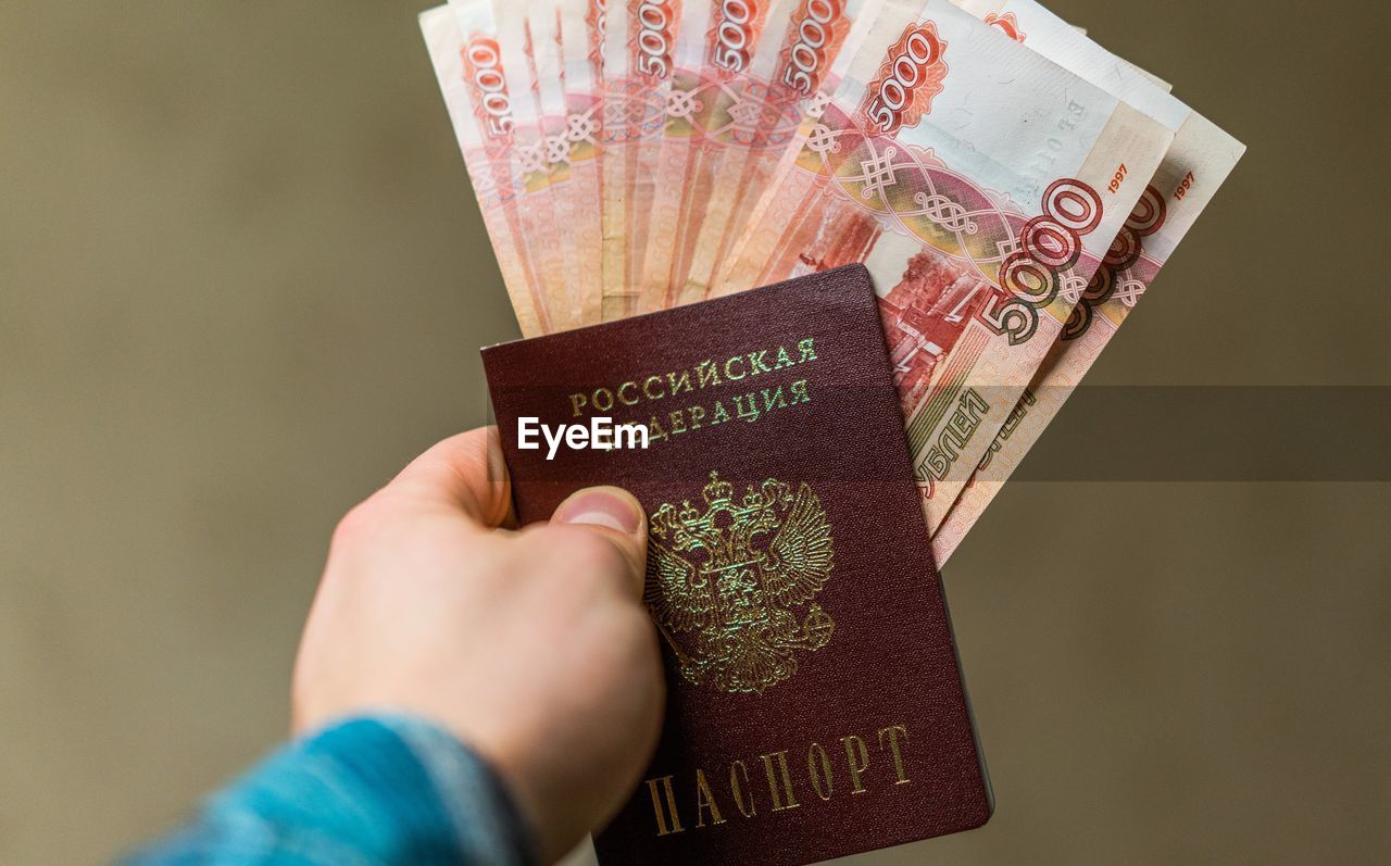 Close-up of man holding money and passport against brown background