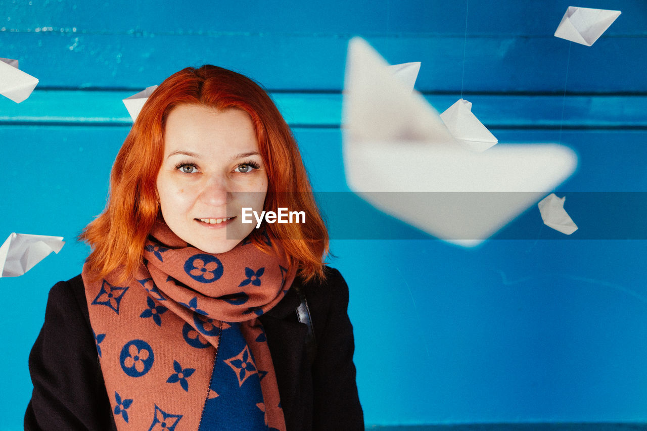 Smiling woman with paper boats hanging against blue wall