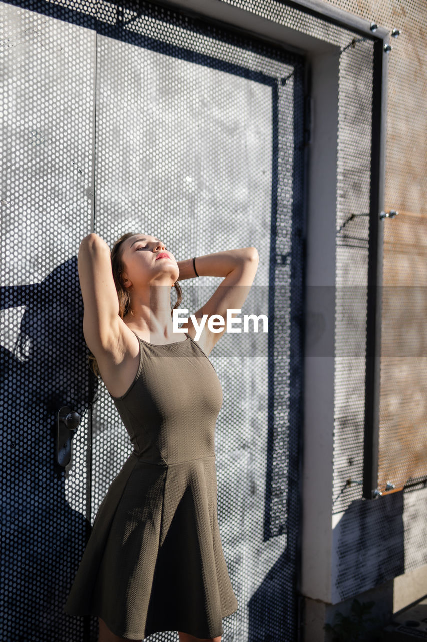 Thoughtful young woman with eyes closed while standing against warehouse