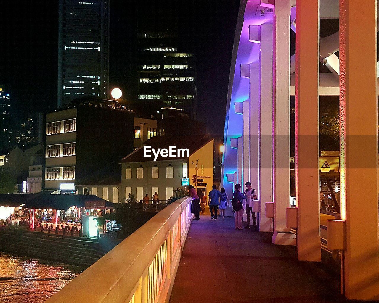 People on illuminated footbridge over river at night