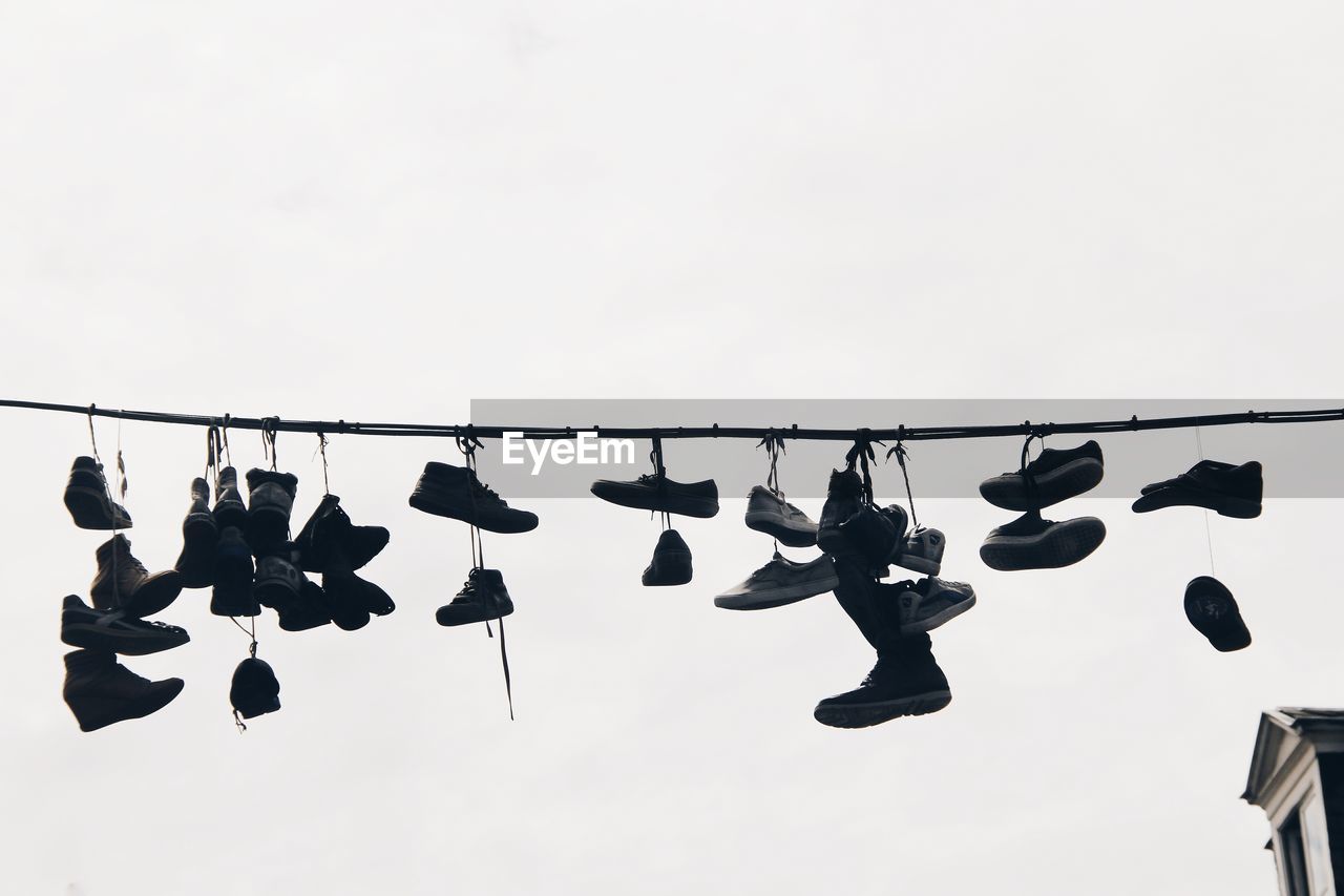 Low angle view of shoes hanging on rope against sky