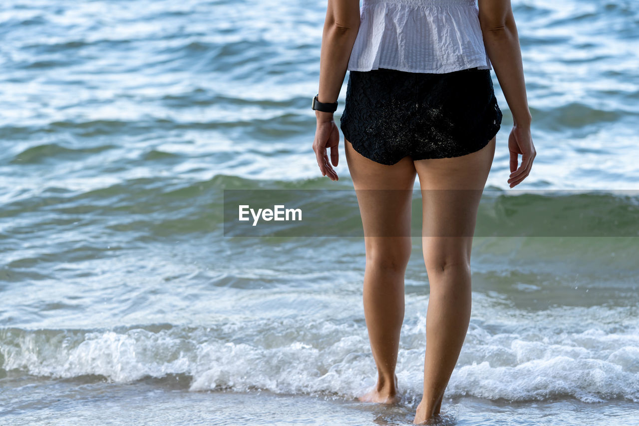 REAR VIEW OF WOMAN STANDING IN SEA