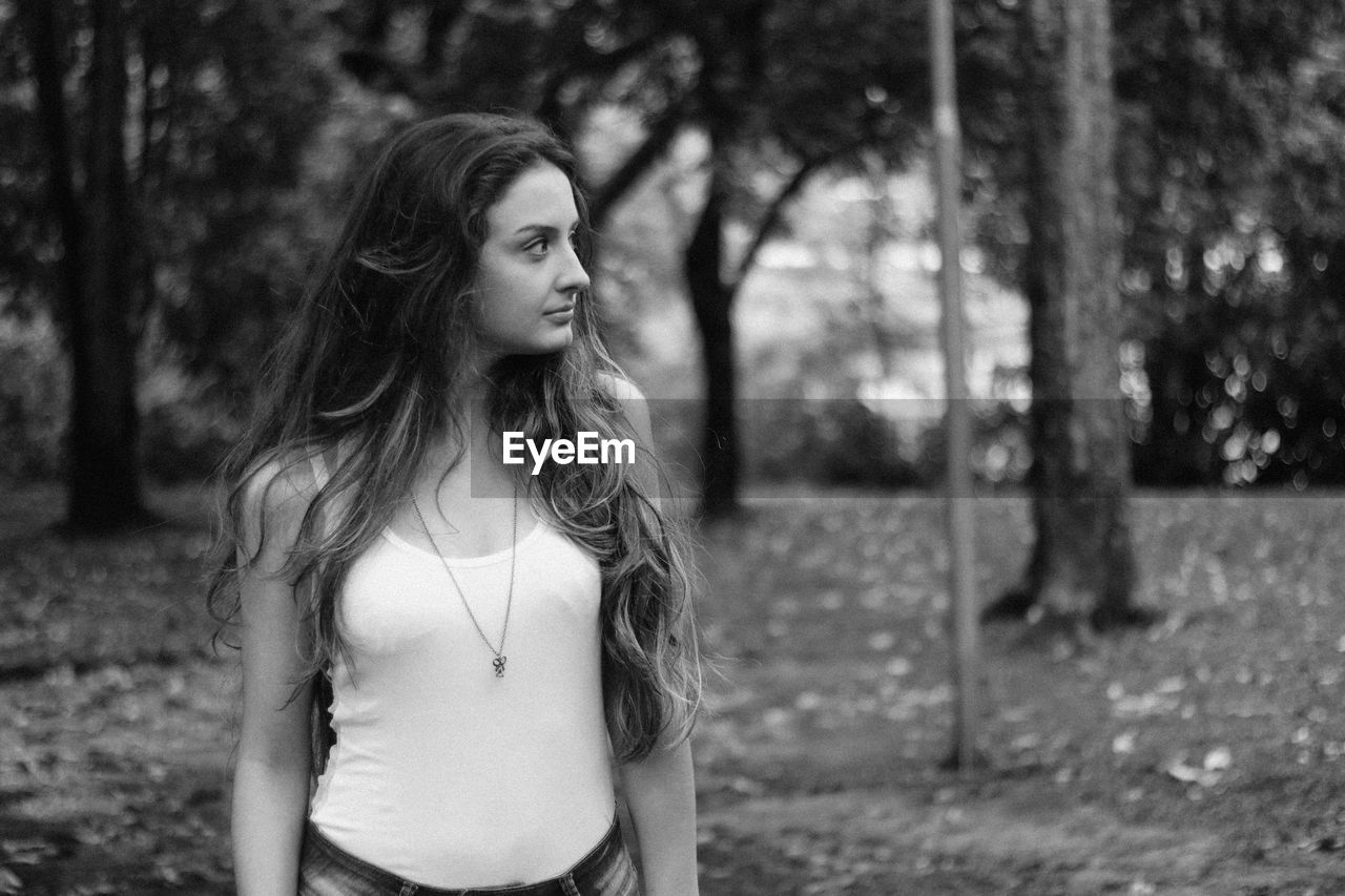 Beautiful young woman looking away while standing against trees