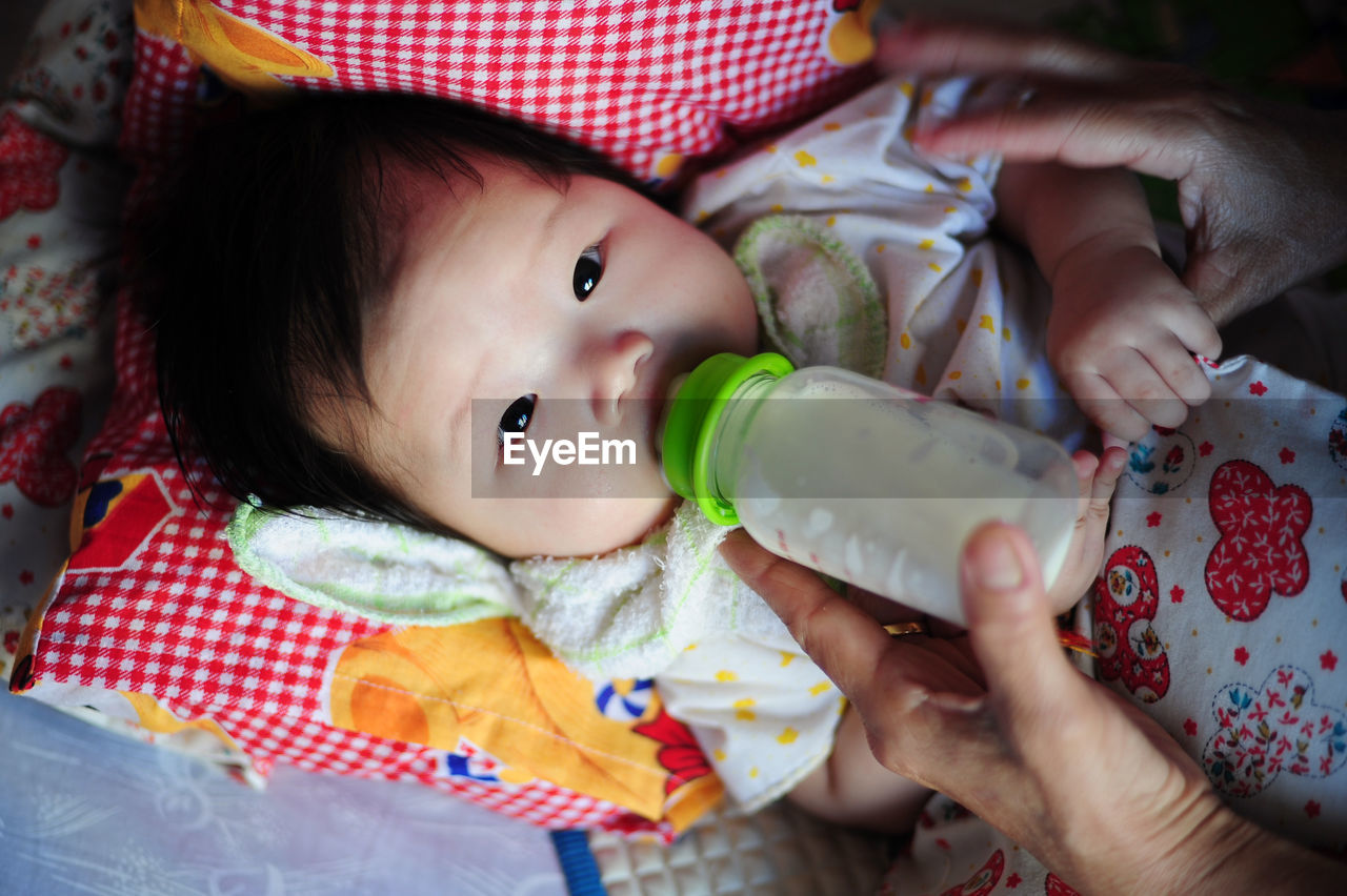 Cropped image of hand feeding milk to baby with bottle