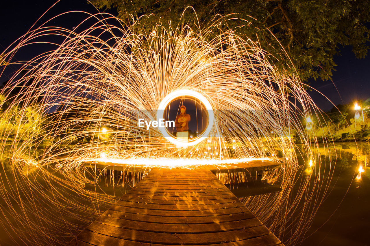 Man spinning wire wool on pier over lake at night