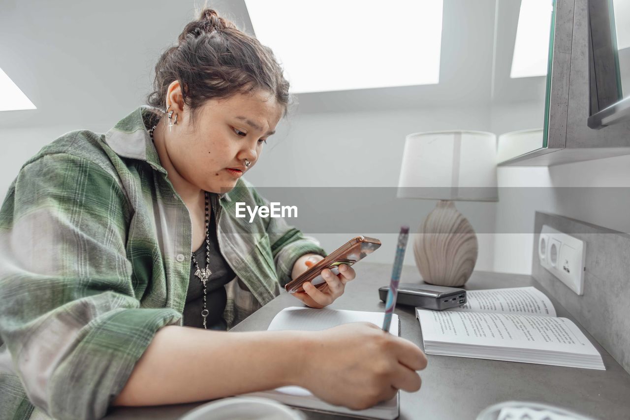 Asian student juggles between phone, handwritten notes, multitasking skills in learning environments