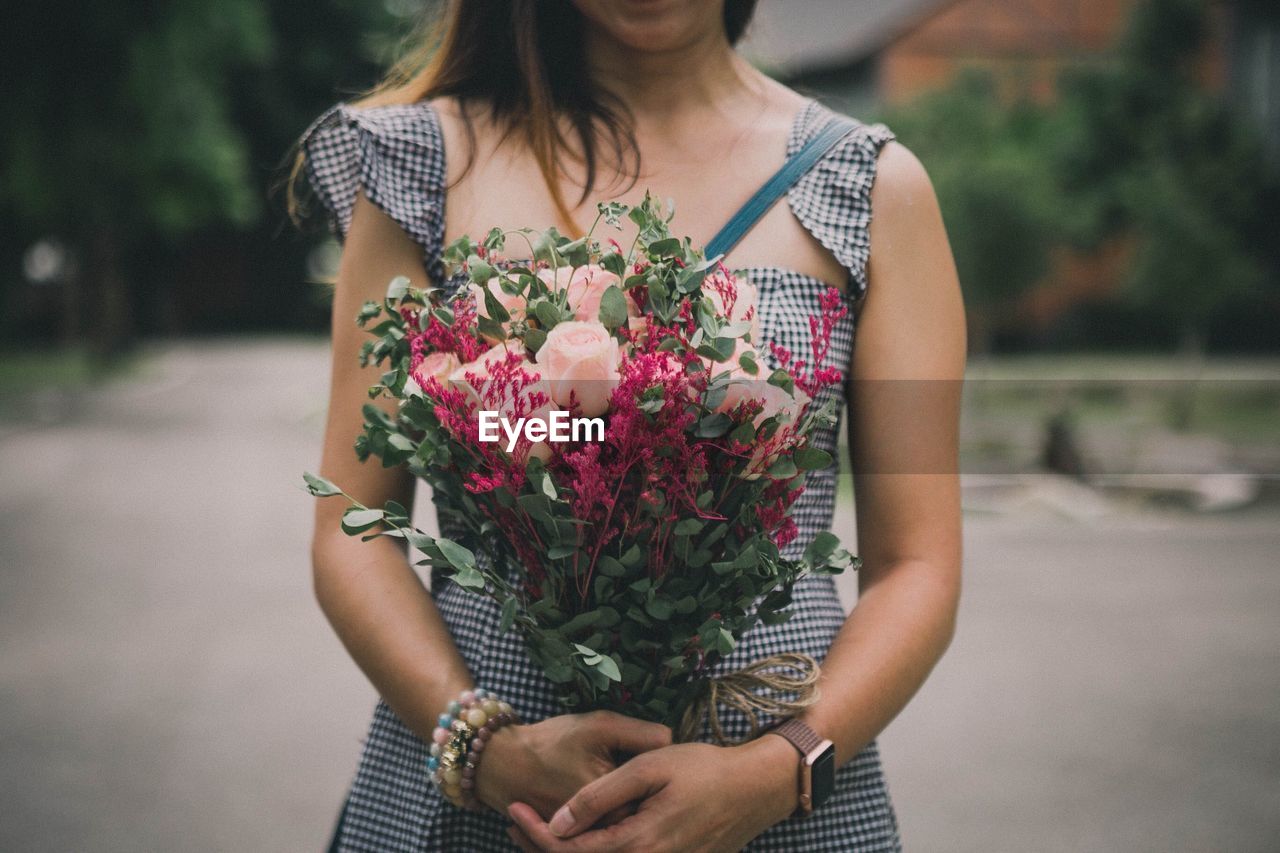 Midsection of woman holding flower bouquet while standing on footpath