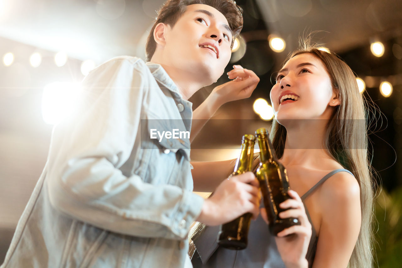 Low angle view of couple holding beer bottles while looking away during party