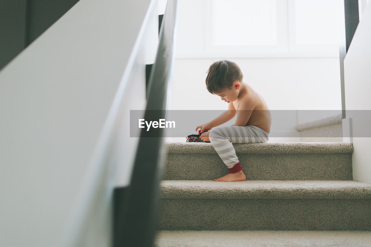 Shirtless boy sitting on staircase at home