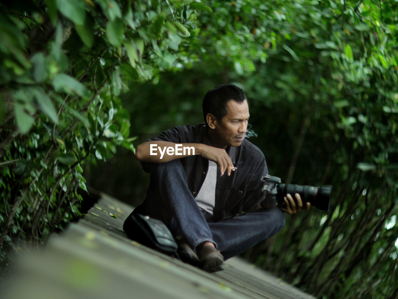 Young man looking down while sitting on tree