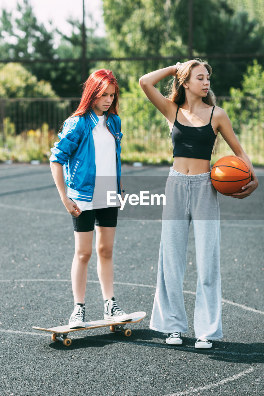 Portrait of two teenage girls with a basketball and a skateboard on a sports field