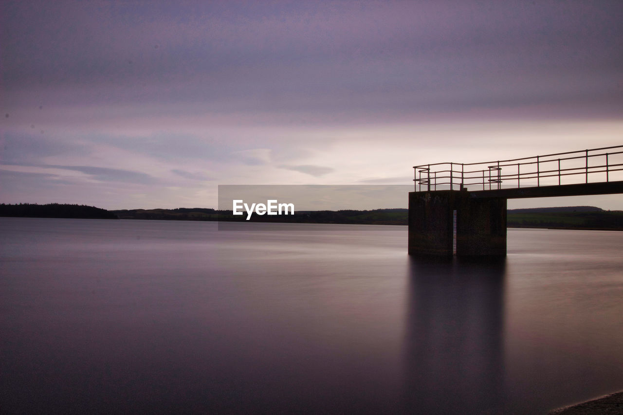 Bridge over lake against cloudy sky during sunset