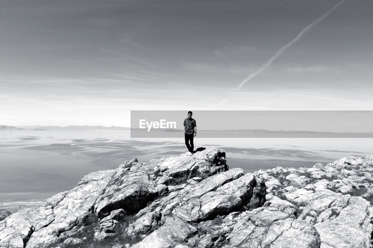 Full length of mid adult man standing on rock by sea against sky