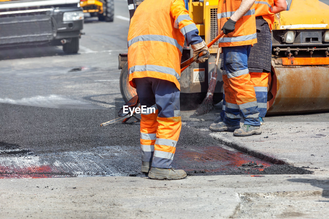 A group of road workers are repairing a section of the carriageway by rolling up fresh asphalt.