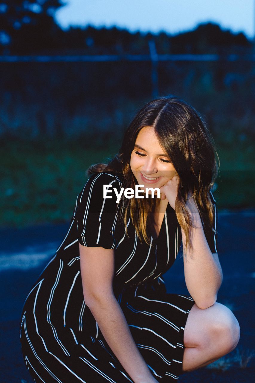 Cheerful beautiful woman crouching on road at dusk