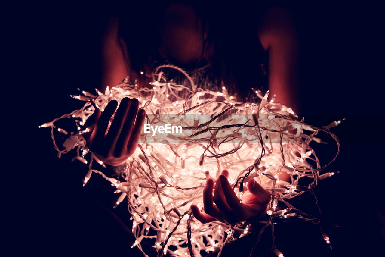 Teenage girl with illuminated fairy lights in darkroom at home