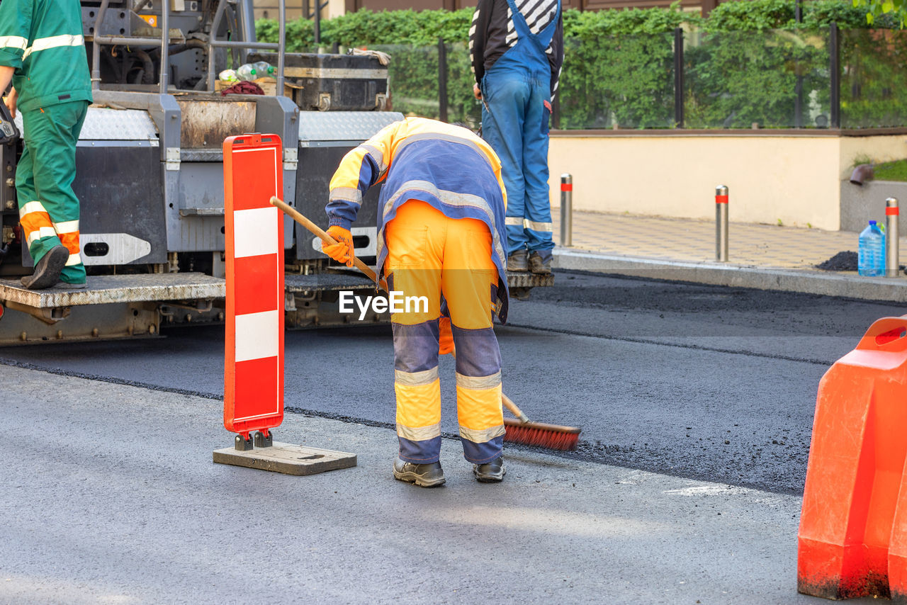 A team of road builders on an asphalt paver carefully lay fresh asphalt on the carriageway.