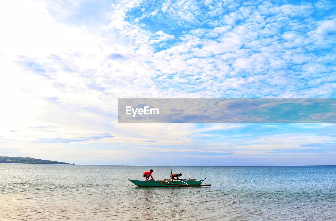 MEN IN BOAT ON SEA AGAINST SKY