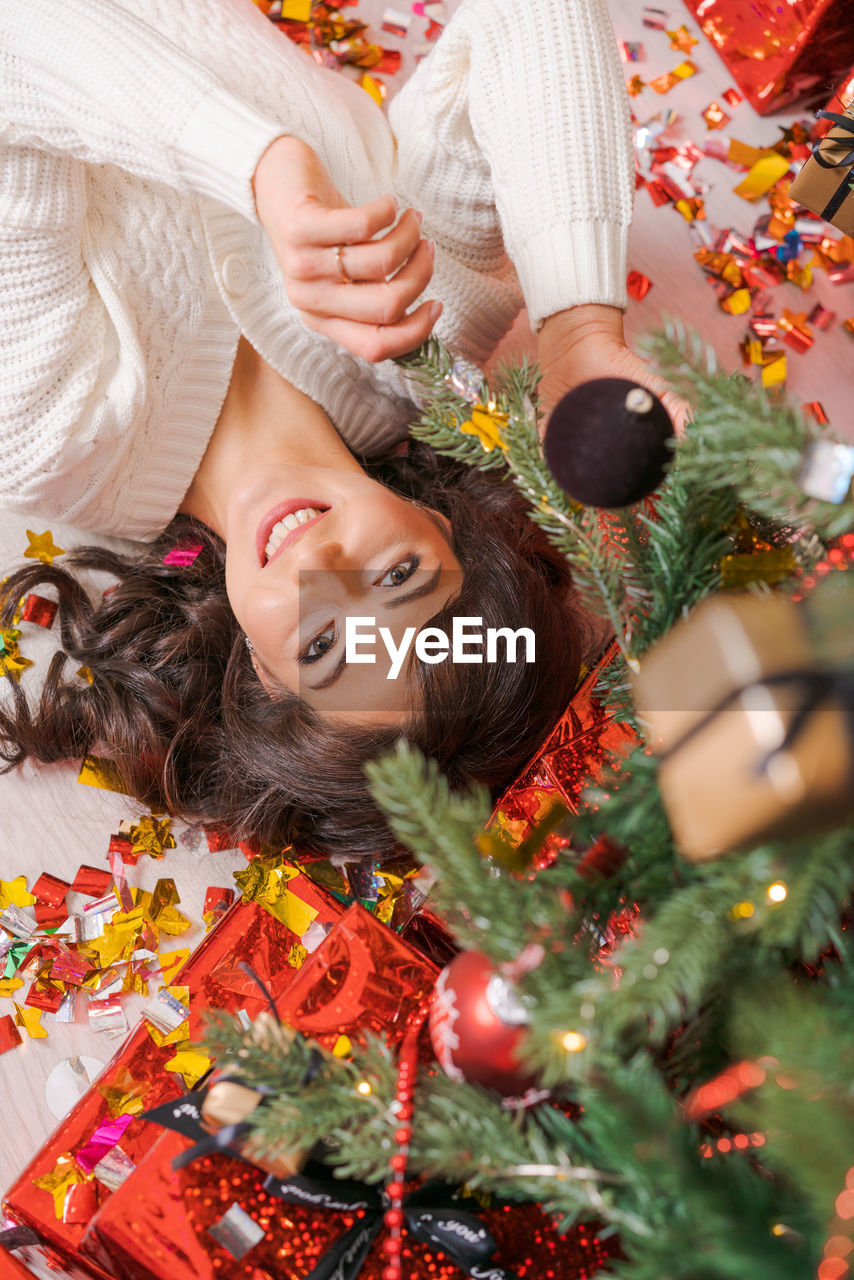 High angle view young woman lying on floor near christmas tree with gifts. top