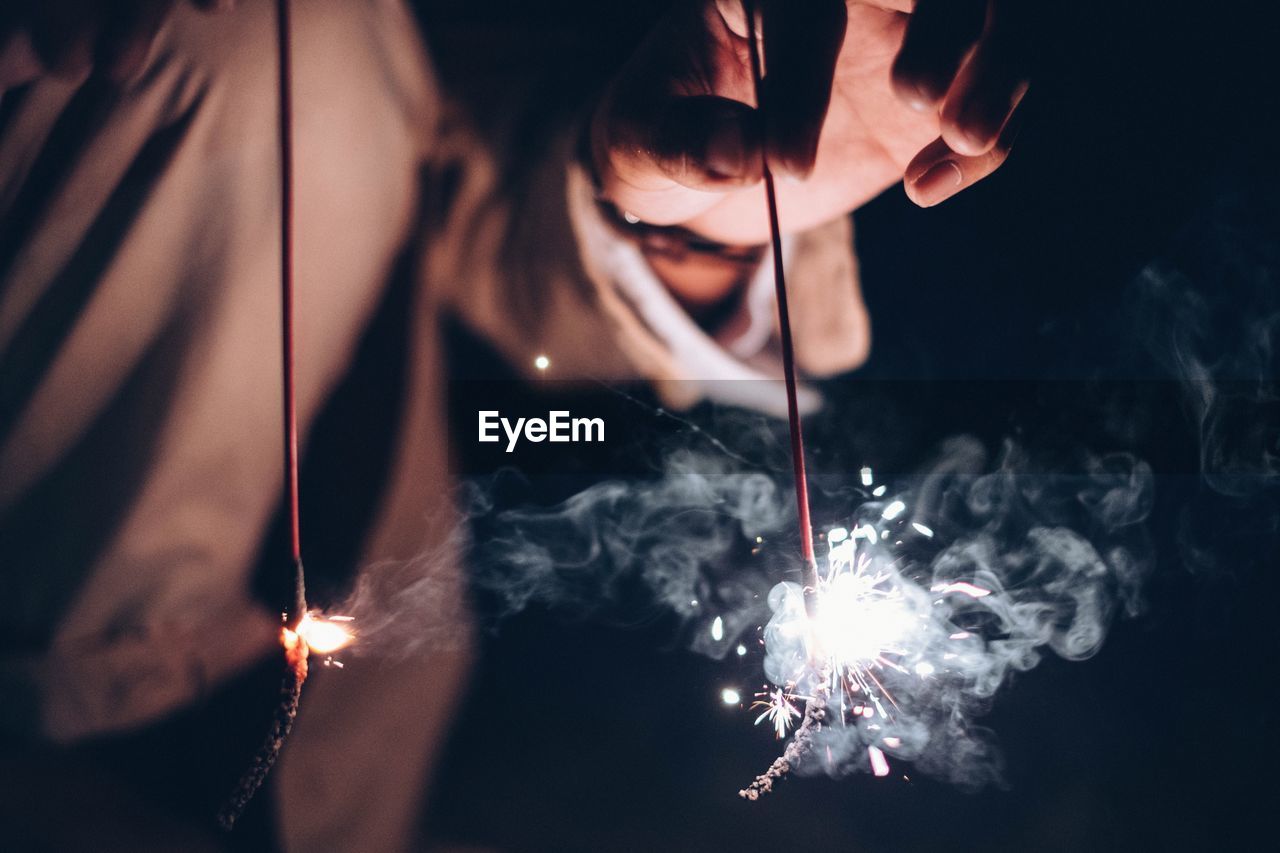 Midsection of woman holding lit sparklers at night