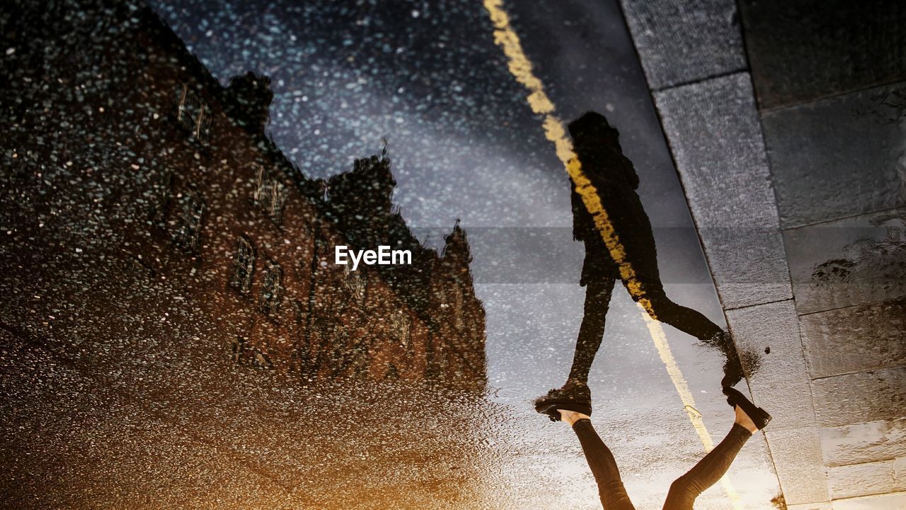 Low section of woman walking on wet street with reflection