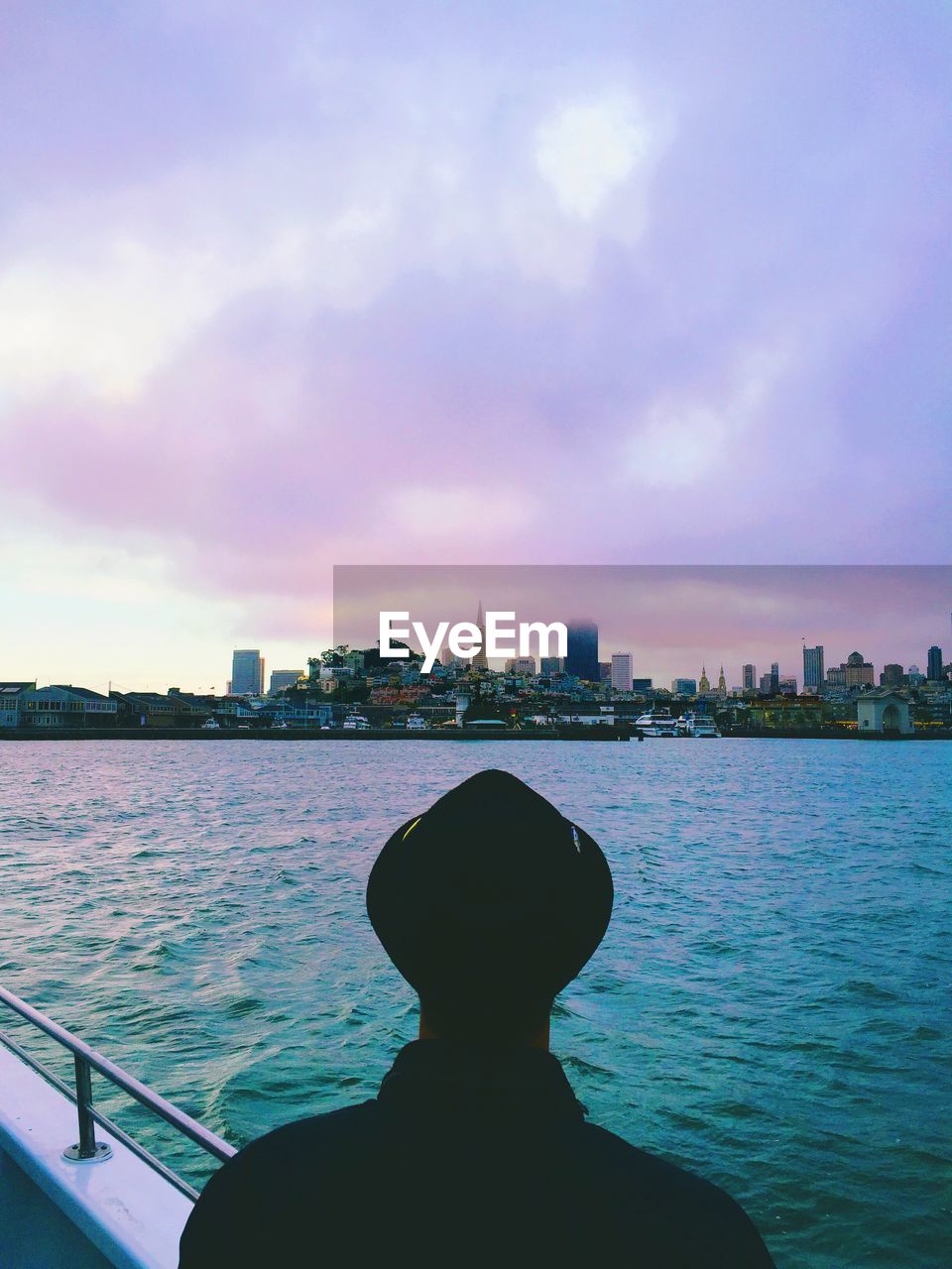 Rear view of man sailing in sea while looking at city against cloudy sky