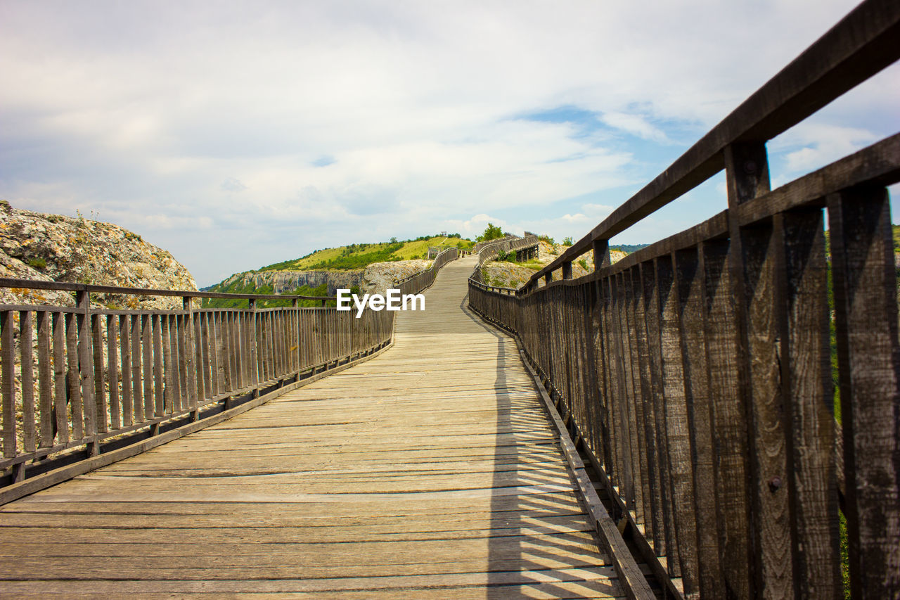 Wooden footbridge on boardwalk against sky