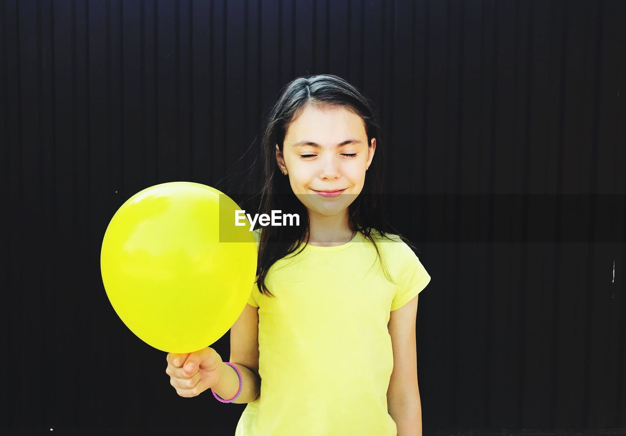 Smiling girl holding yellow balloon against black background