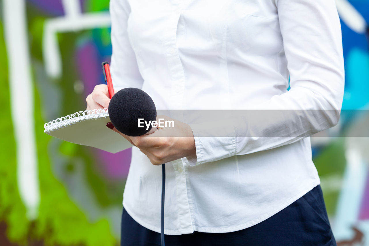 News reporter or tv journalist at press conference, holding microphone and writing notes