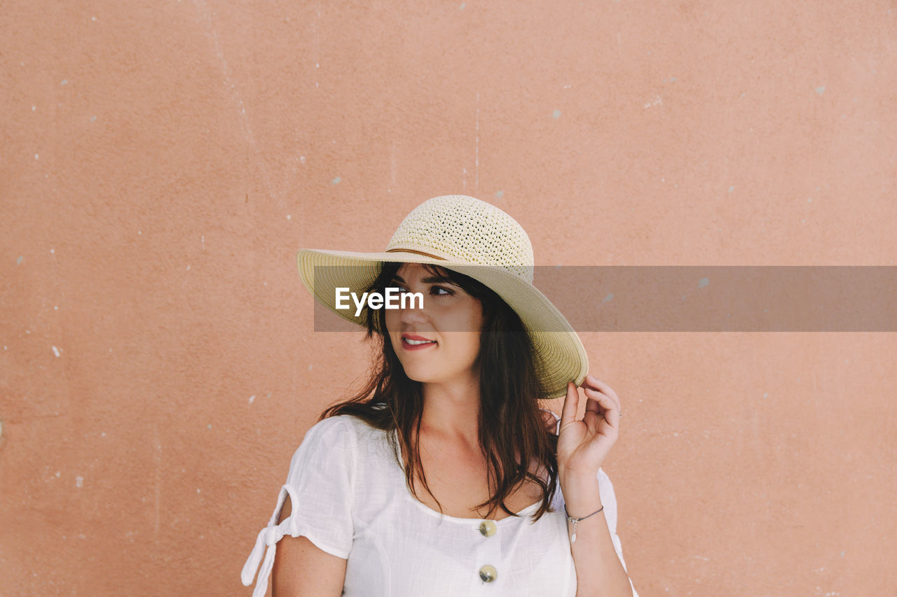 Portrait of beautiful young woman wearing summer clothes, standing in front of pastel orange wall