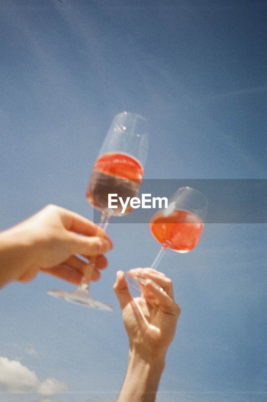 Hand holding wineglass against blue sky during summertime. shot on 35mm kodak gold 200 film.