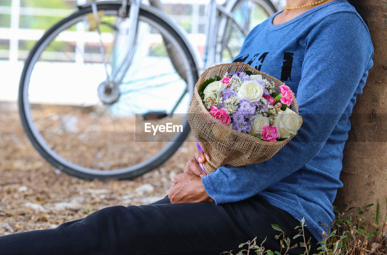 Midsection of woman holding bouquet while sitting on field