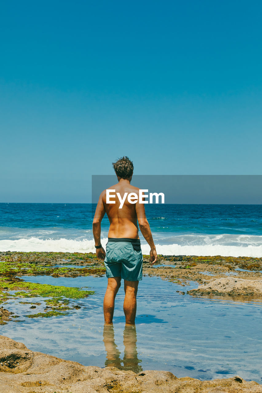 Young man standing in water looking out to ocean from bluffs in baja.