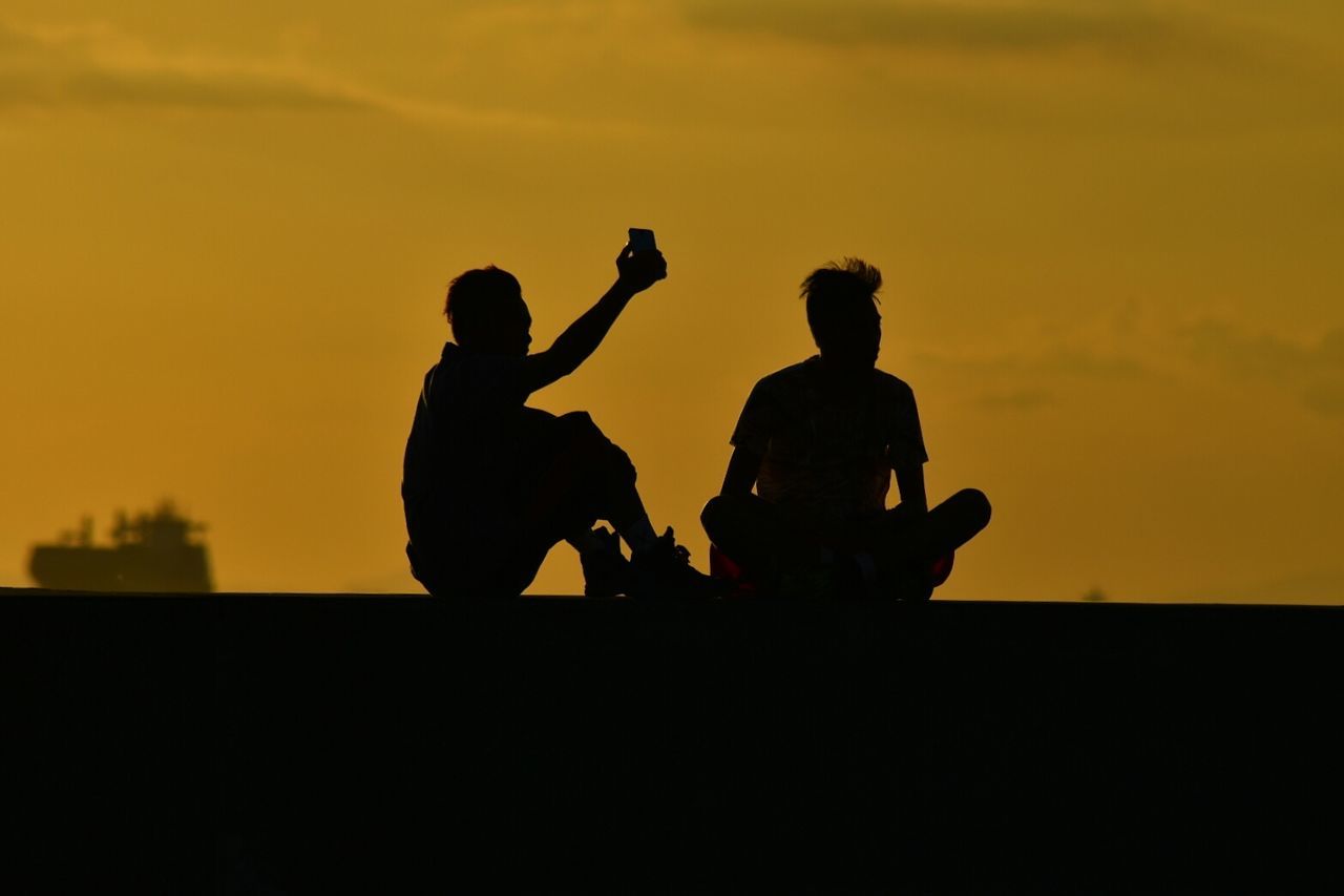 Silhouette man taking selfie with friend during sunset