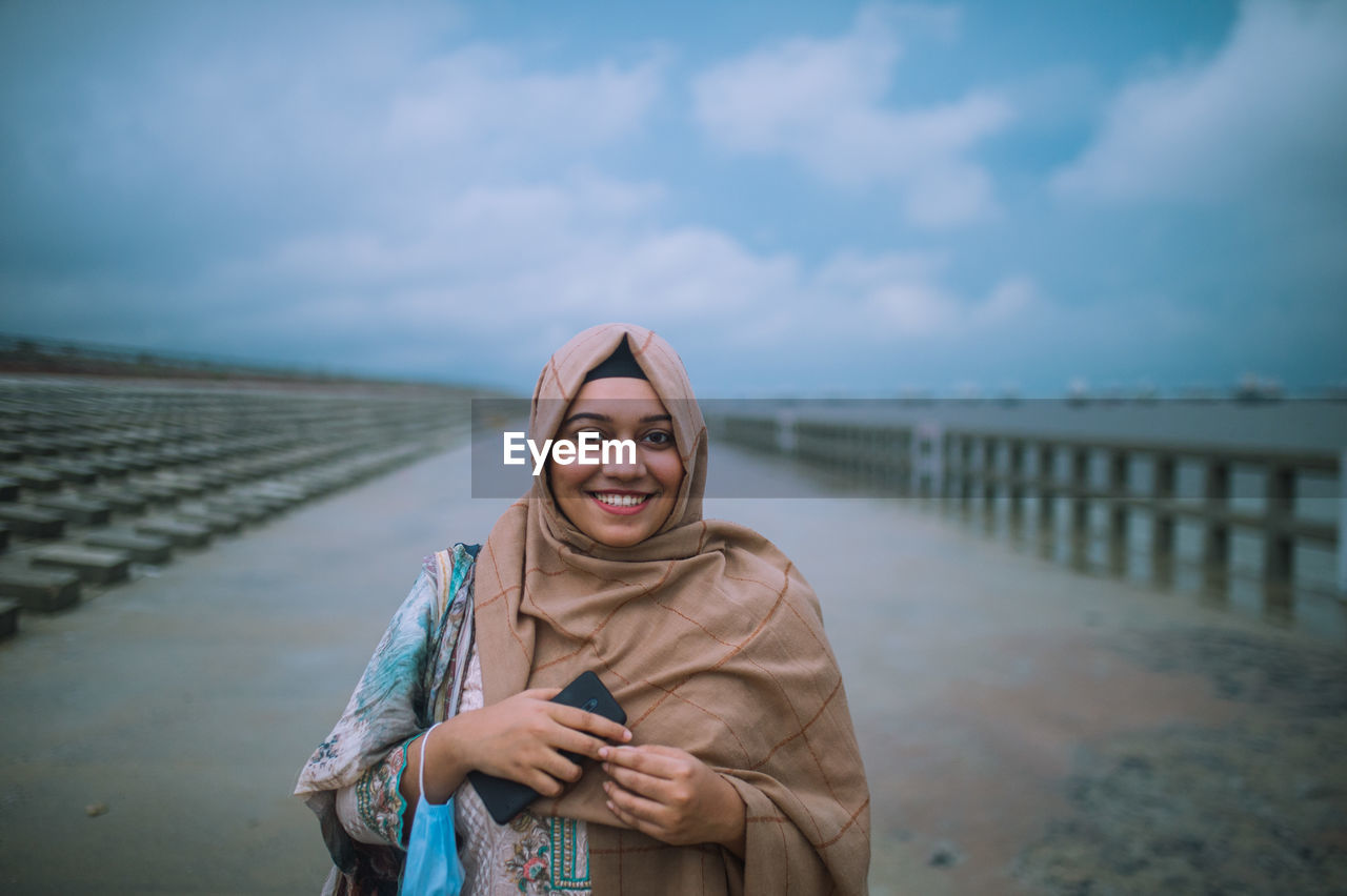 Portrait of smiling young woman standing against sky