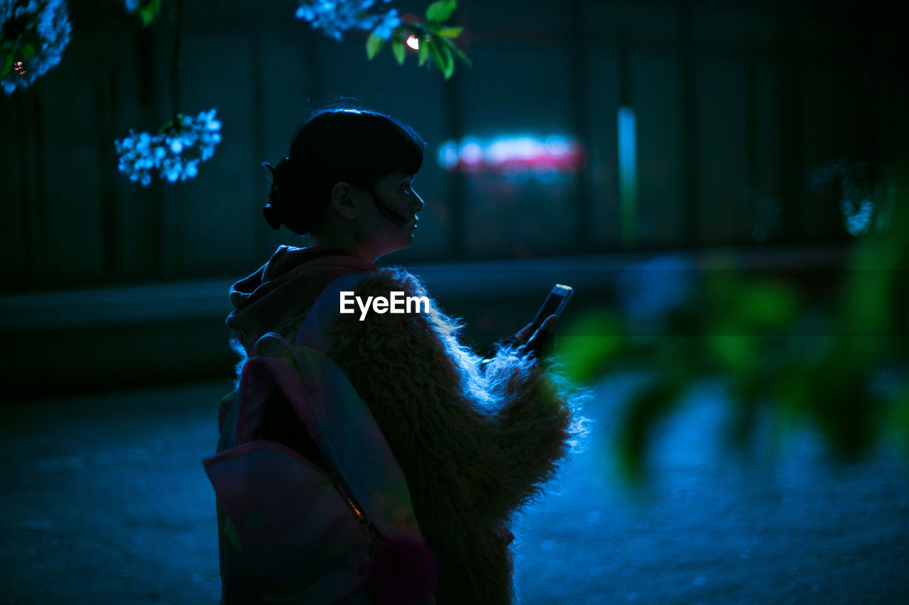 Woman holding phone while standing outdoors at night