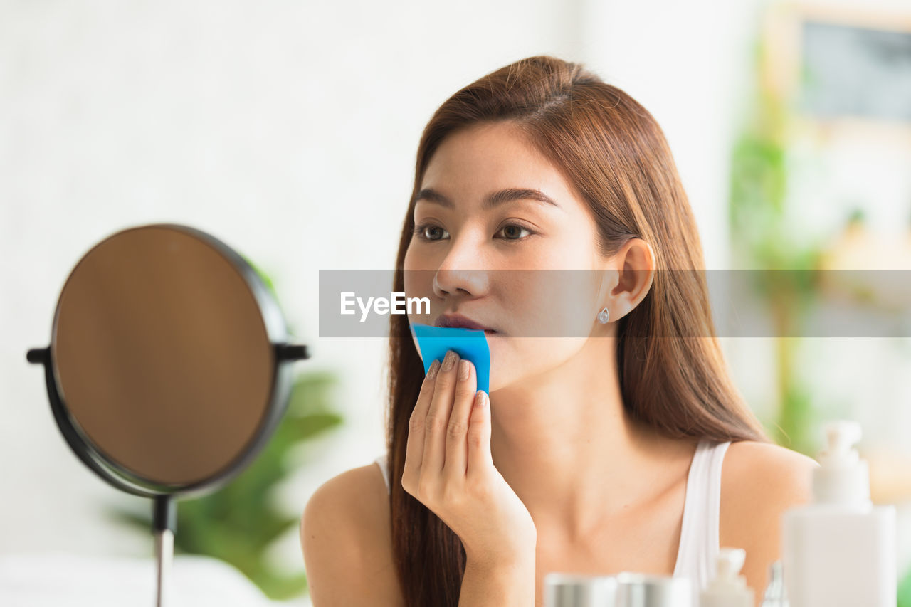 PORTRAIT OF YOUNG WOMAN HOLDING CAMERA IN KITCHEN