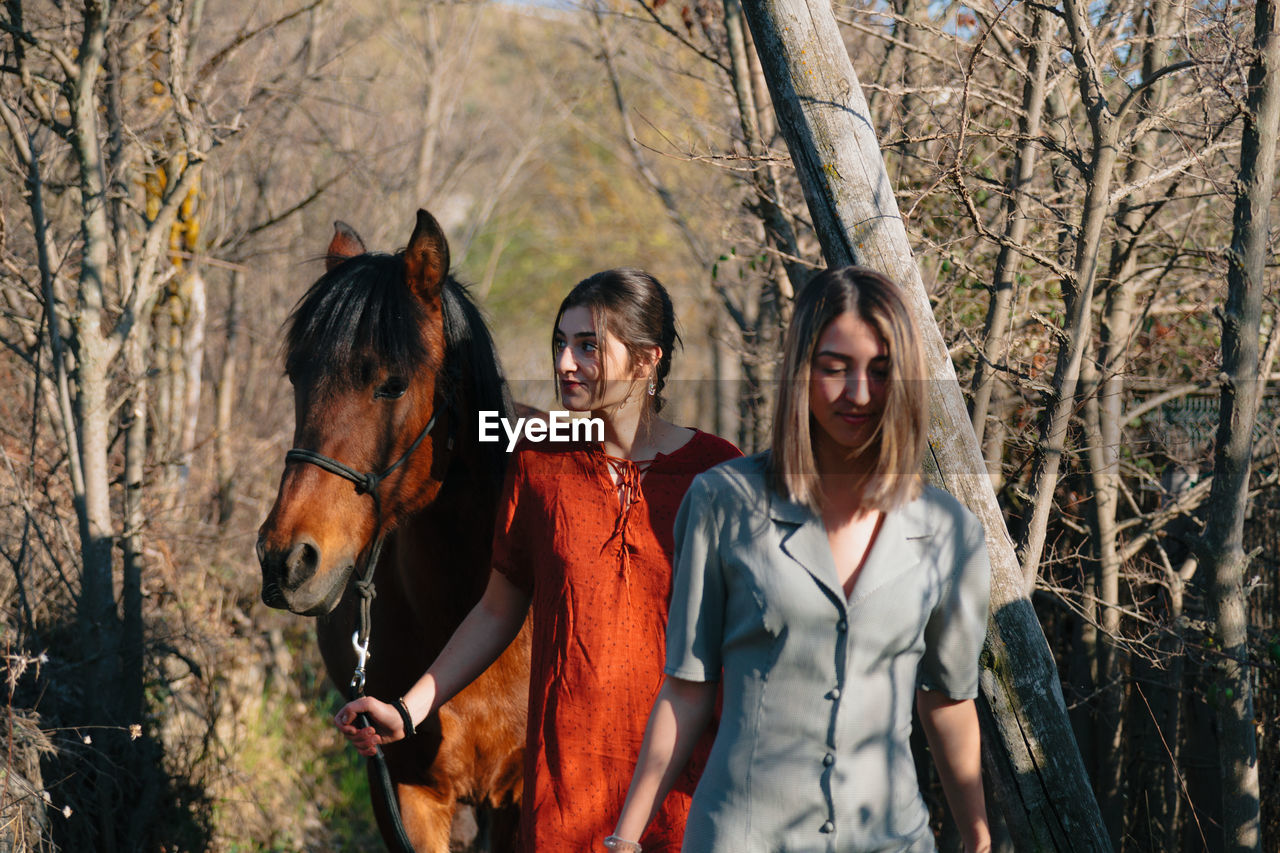 Young women with horse walking amidst trees