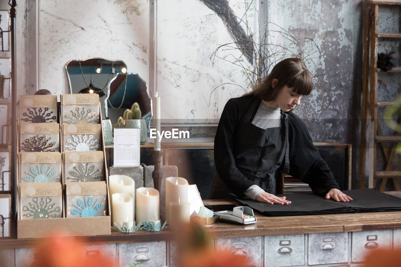 Confident young female owner looking at wrapping paper on counter in store