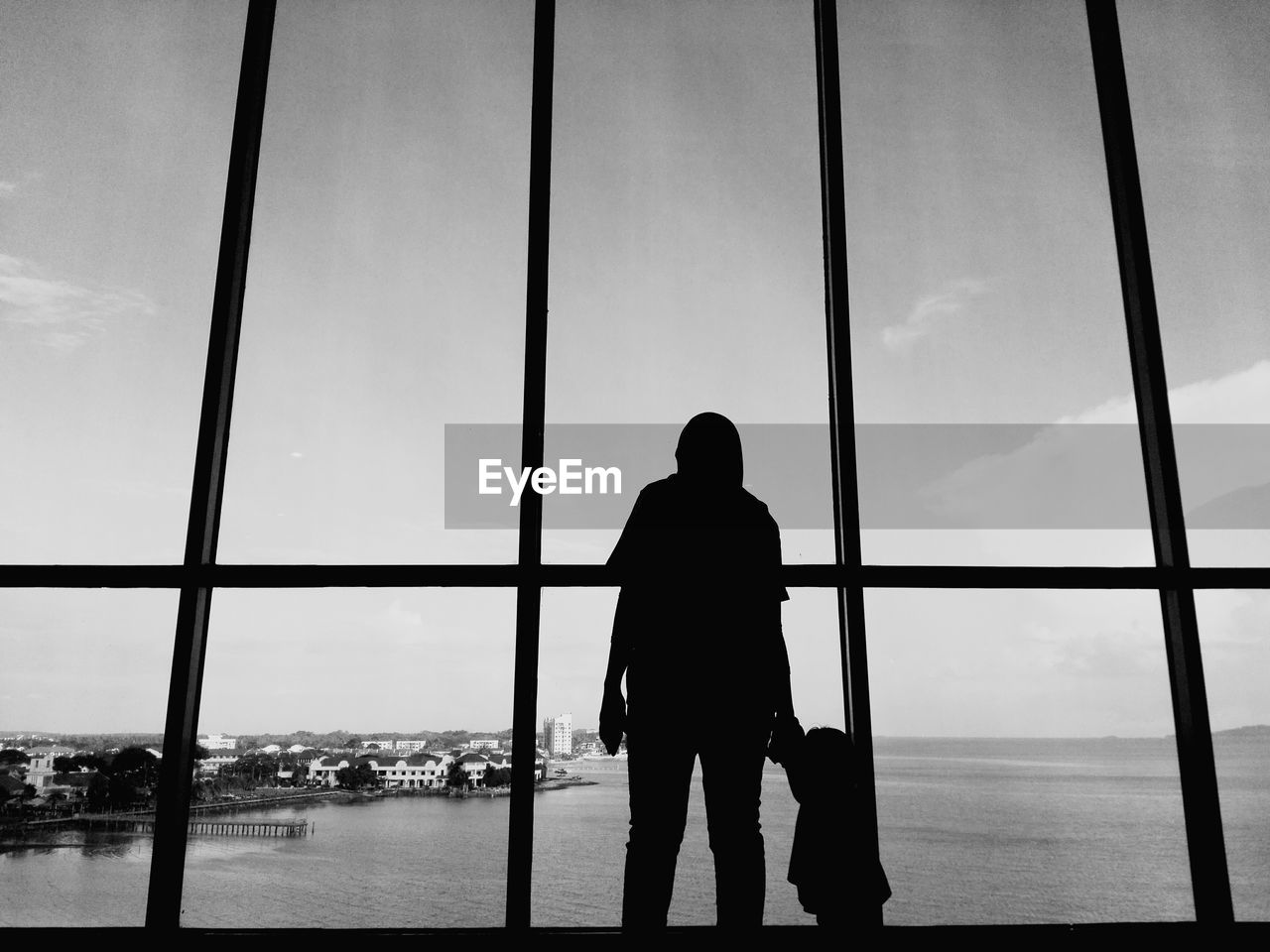 Silhouette mother with daughter standing by window against sea