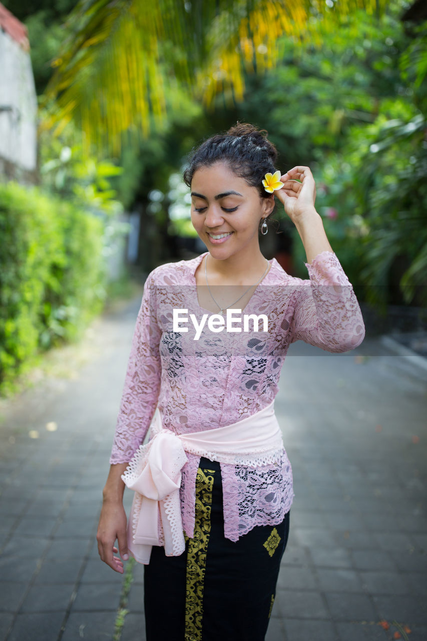 Beautiful young woman wearing flower on ear while standing on footpath