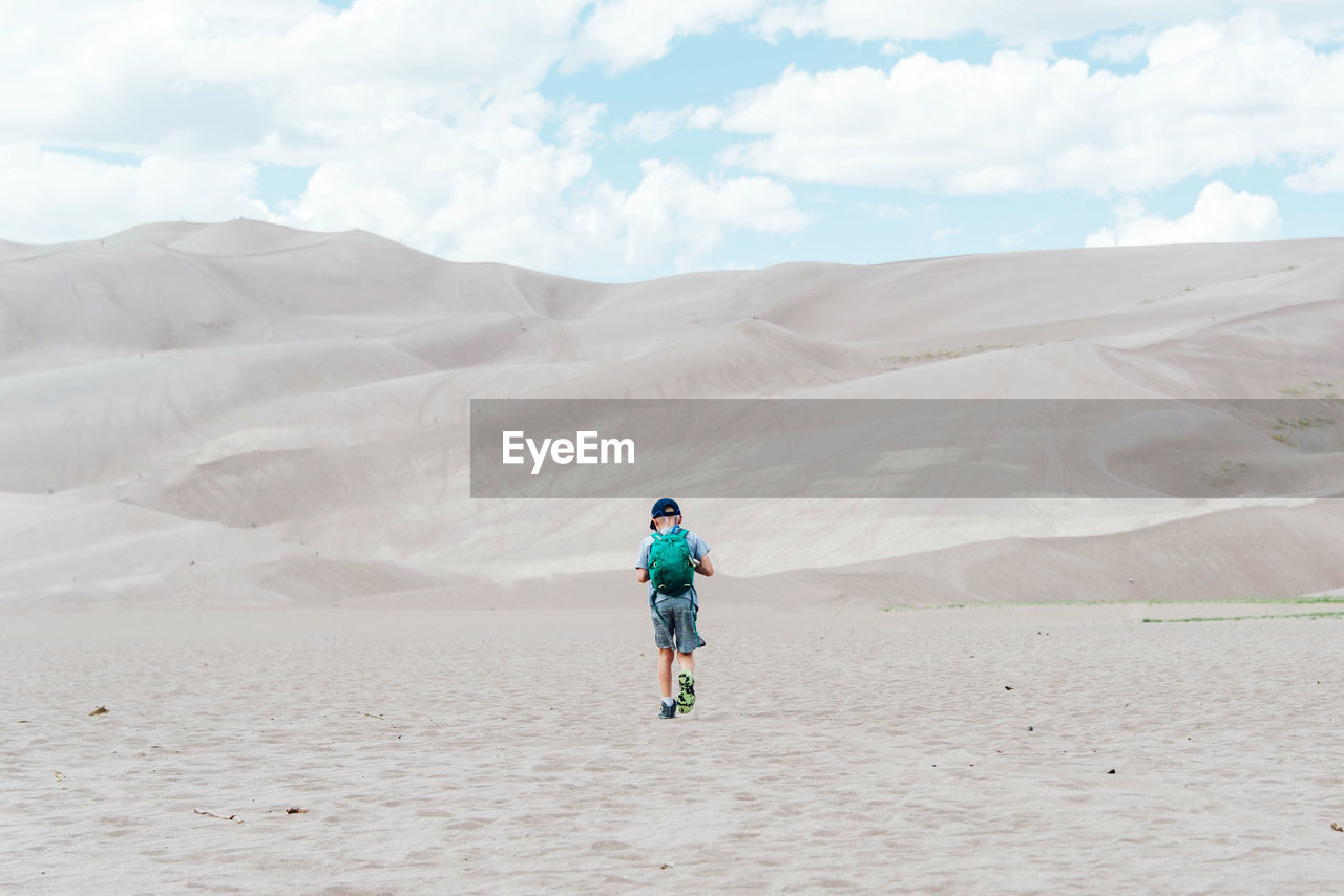 Rear view of boy on sand against sky