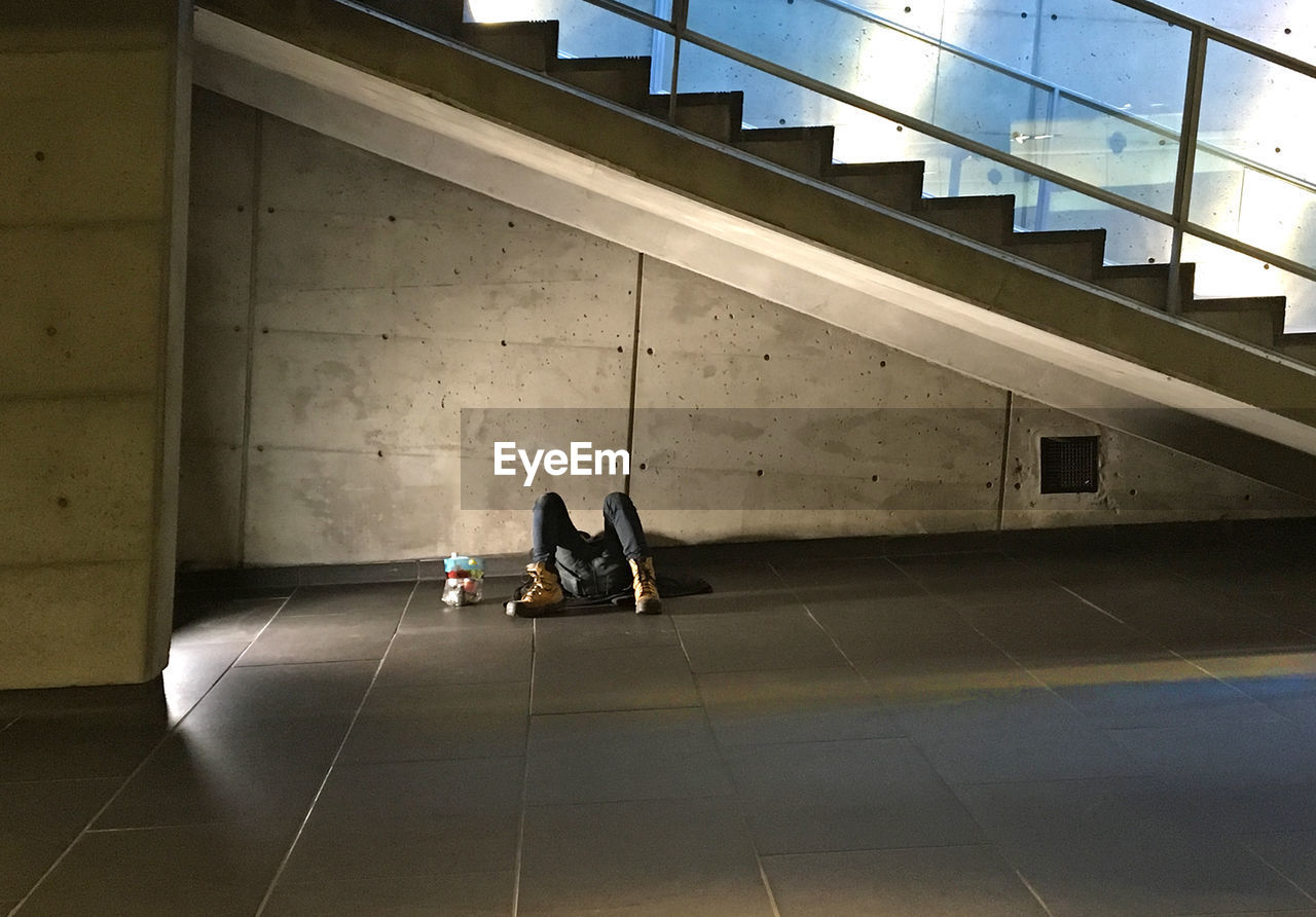 Homeless man sleeping on floor below staircase in building