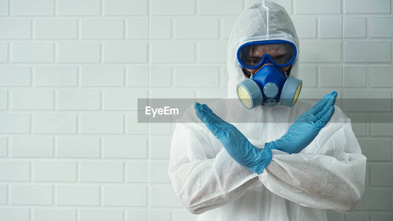 PORTRAIT OF MAN WEARING MASK STANDING AGAINST WHITE WALL