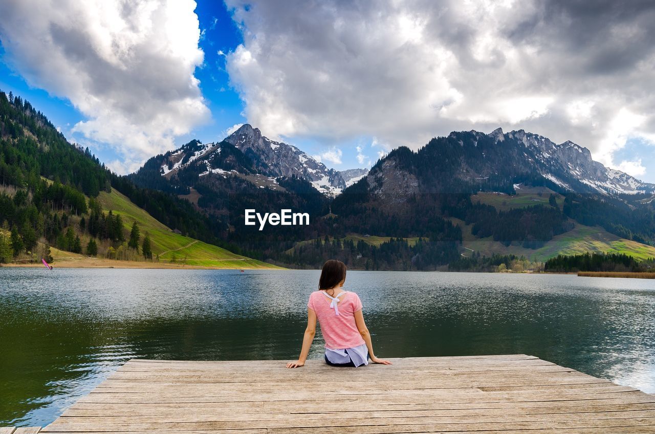 Rear view of girl by lake against cloudy sky