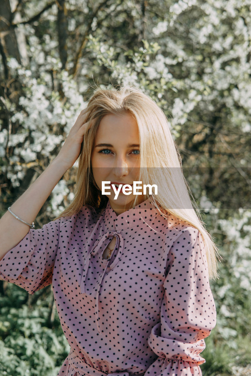 Blonde girl on a spring walk in the garden with cherry blossoms. female portrait, close-up. 