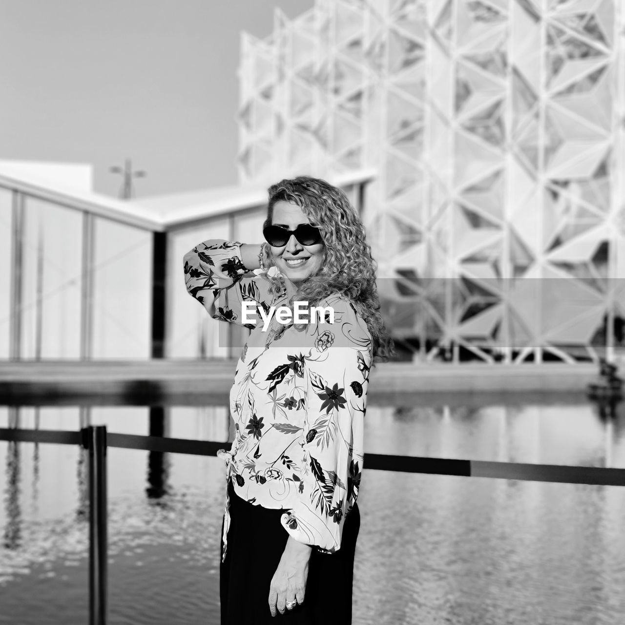 A lady wearing sunglasses standing by railing against water