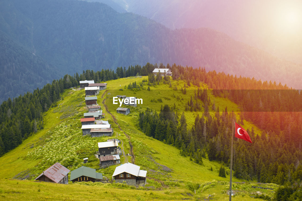 mountain range, scenics - nature, environment, mountain, landscape, land, plant, beauty in nature, tree, nature, forest, valley, meadow, house, mountain pass, ridge, rural scene, tranquility, grass, fog, sun, architecture, no people, sky, building, pinaceae, tranquil scene, field, hut, green, pine tree, coniferous tree, non-urban scene, travel, plateau, sunlight, built structure, idyllic, pine woodland, plain, travel destinations, summer, panoramic, wilderness, outdoors, residential district, transportation, high angle view, woodland, mountain peak, building exterior, agriculture, highland, sunrise, day, tourism, activity, morning, foliage, village, remote, multi colored, environmental conservation, lush foliage, sunbeam, growth, vacation, hill station