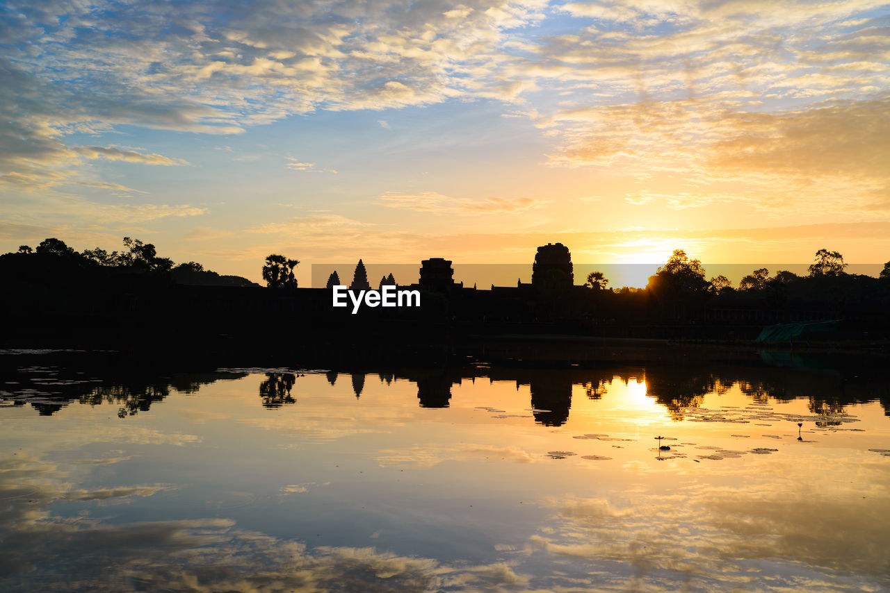 SILHOUETTE BUILDINGS BY LAKE AGAINST ORANGE SKY